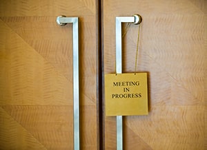 2022 Sign hanging from wooden doors reads "meeting in progress" - Violation Hearing